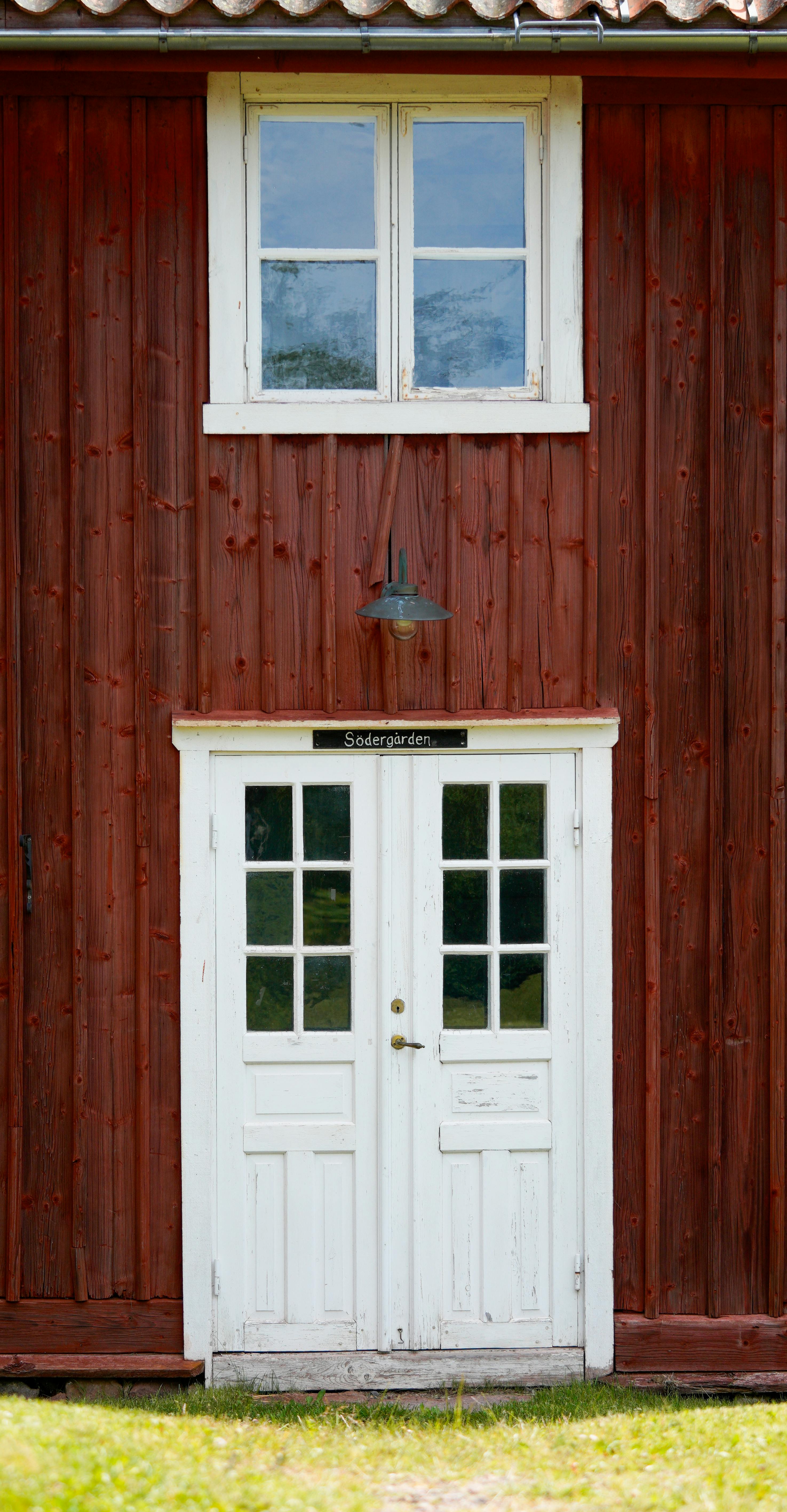 Charming rustic wooden house facade in a rural setting, featuring red walls and white double doors.