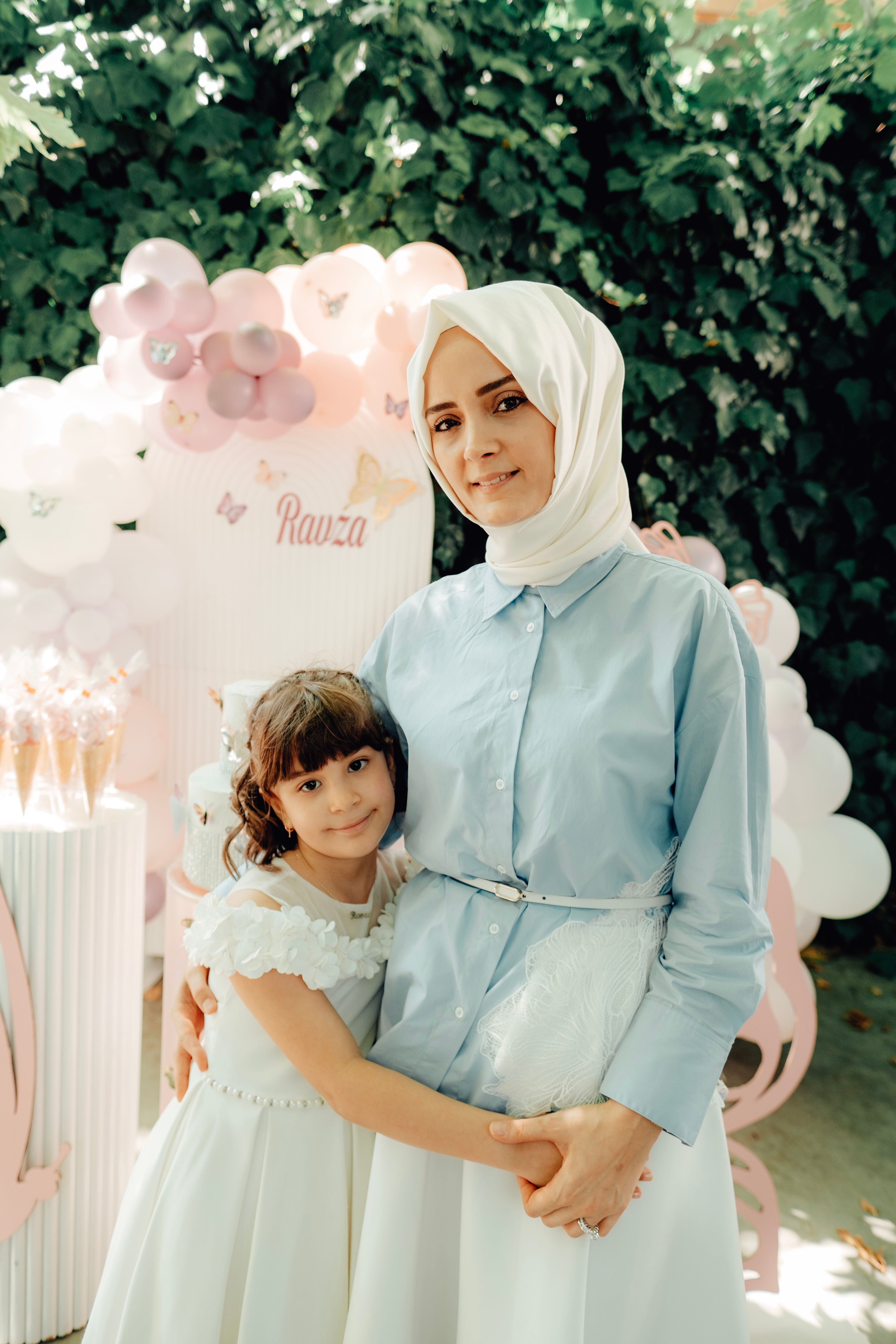 A joyful mother and daughter posing at an outdoor celebration with balloons.