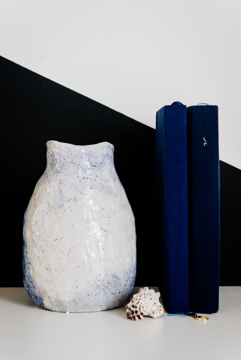 A hand-made jug standing beside two books and a shell