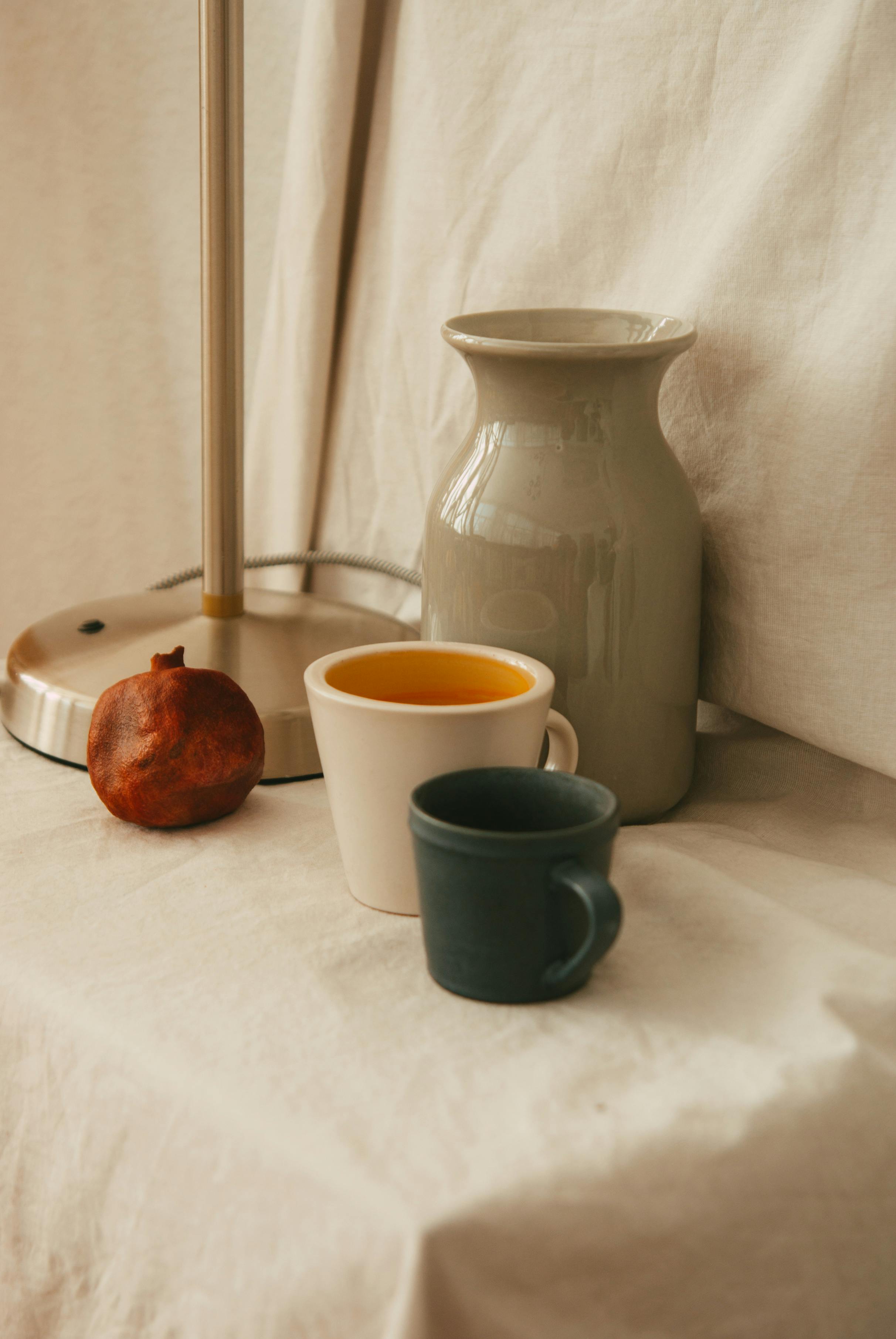 A serene minimalist arrangement of ceramics and a pomegranate on a draped fabric surface.