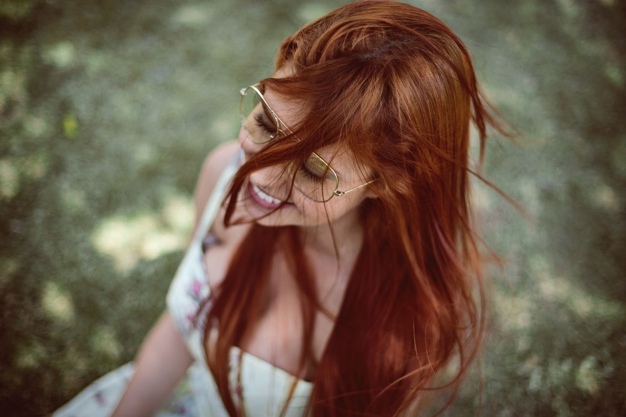 a red haired woman smiling joyfully in an outdoor setting wearing sung