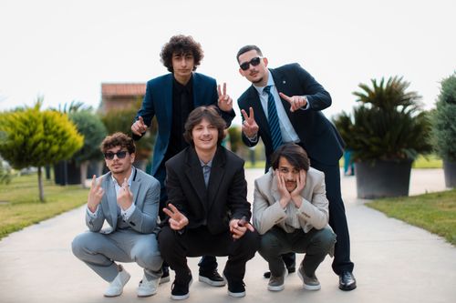 Free Five young men in suits posing playfully in an urban park, showing peace signs. Stock Photo
