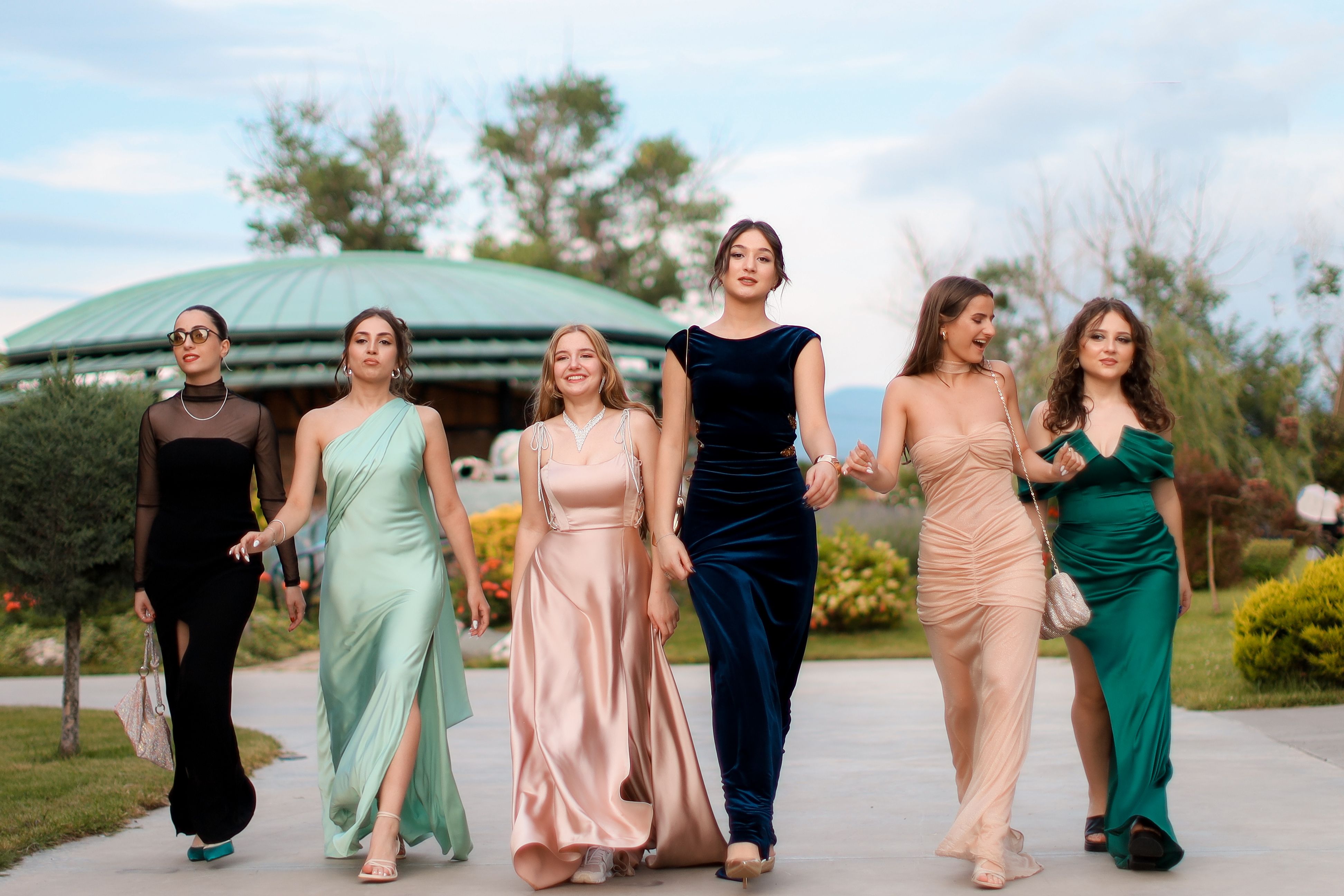 Grupo de jovens femininas vestidas com vestidos elegantes caminhando ao ar livre em uma ocasião social ou evento formal.