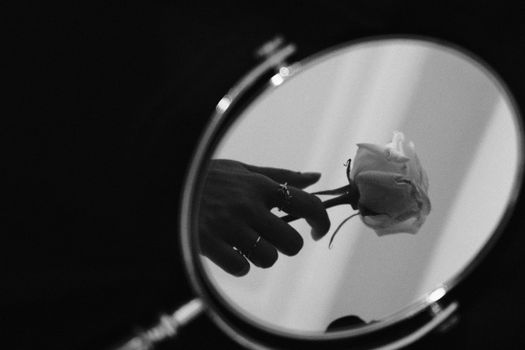 A serene black and white photo of a hand holding a rose reflected in a mirror, conveying elegance.
