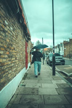 Back view of a woman walking on a city sidewalk holding an umbrella on a rainy day.