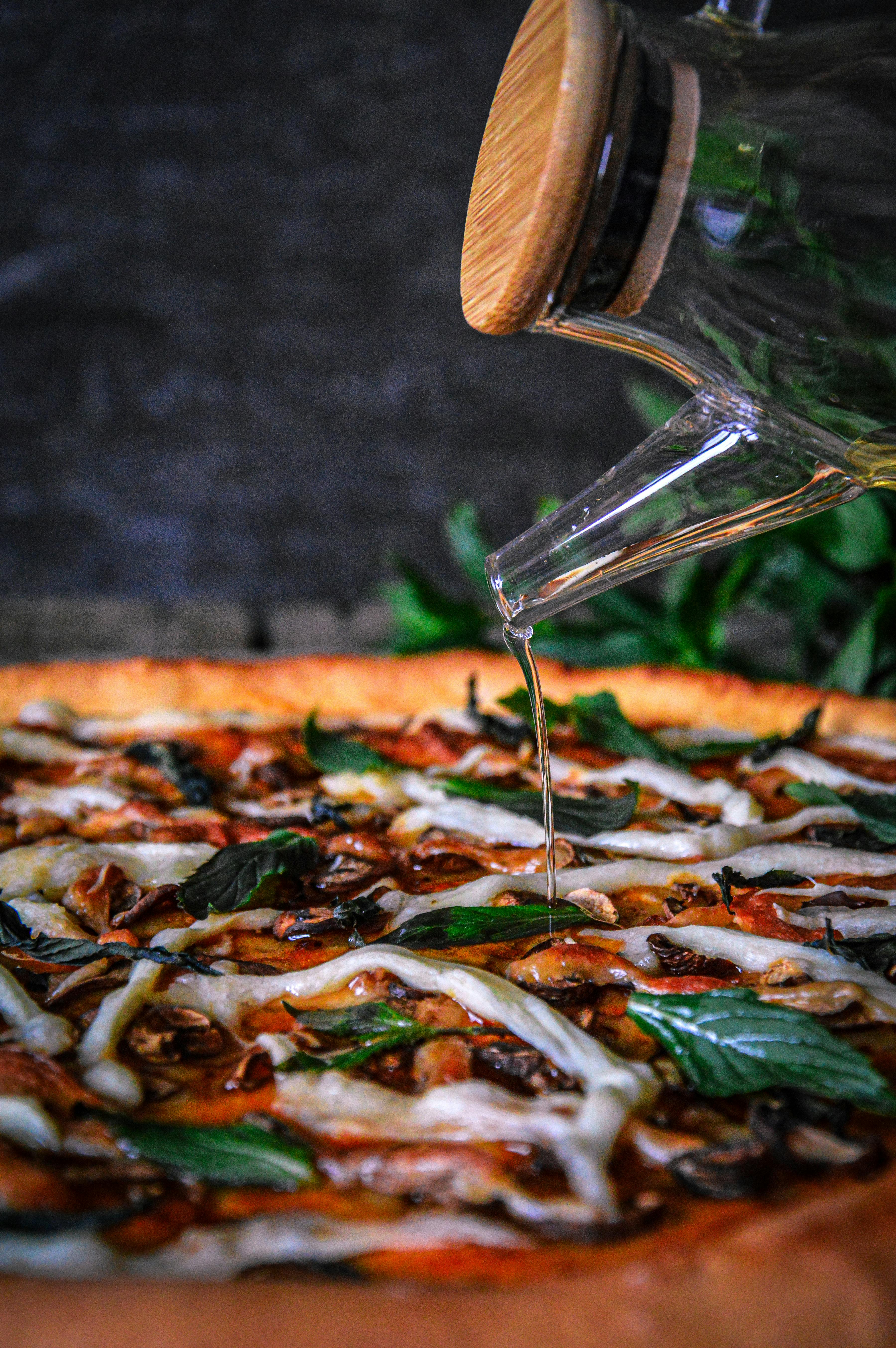 Close-up of olive oil being poured onto a fresh pizza with basil and cheese.