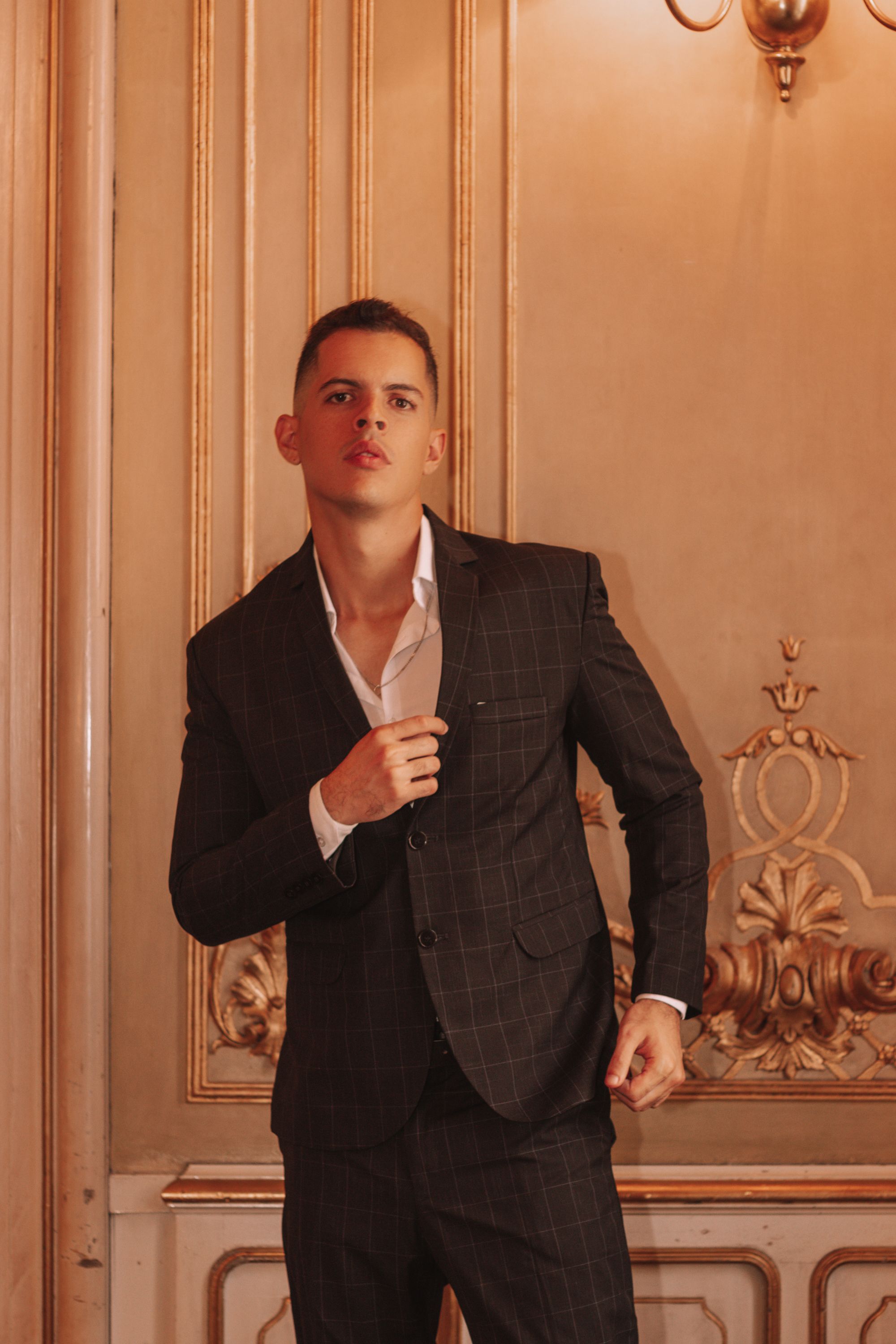 Fashionable portrait of a man in a black suit standing against an ornate wall in Lima, Peru.