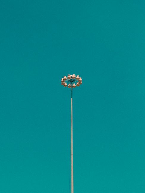 A tall street light pole stands beautifully against a clear turquoise sky, creating a minimalist scene.