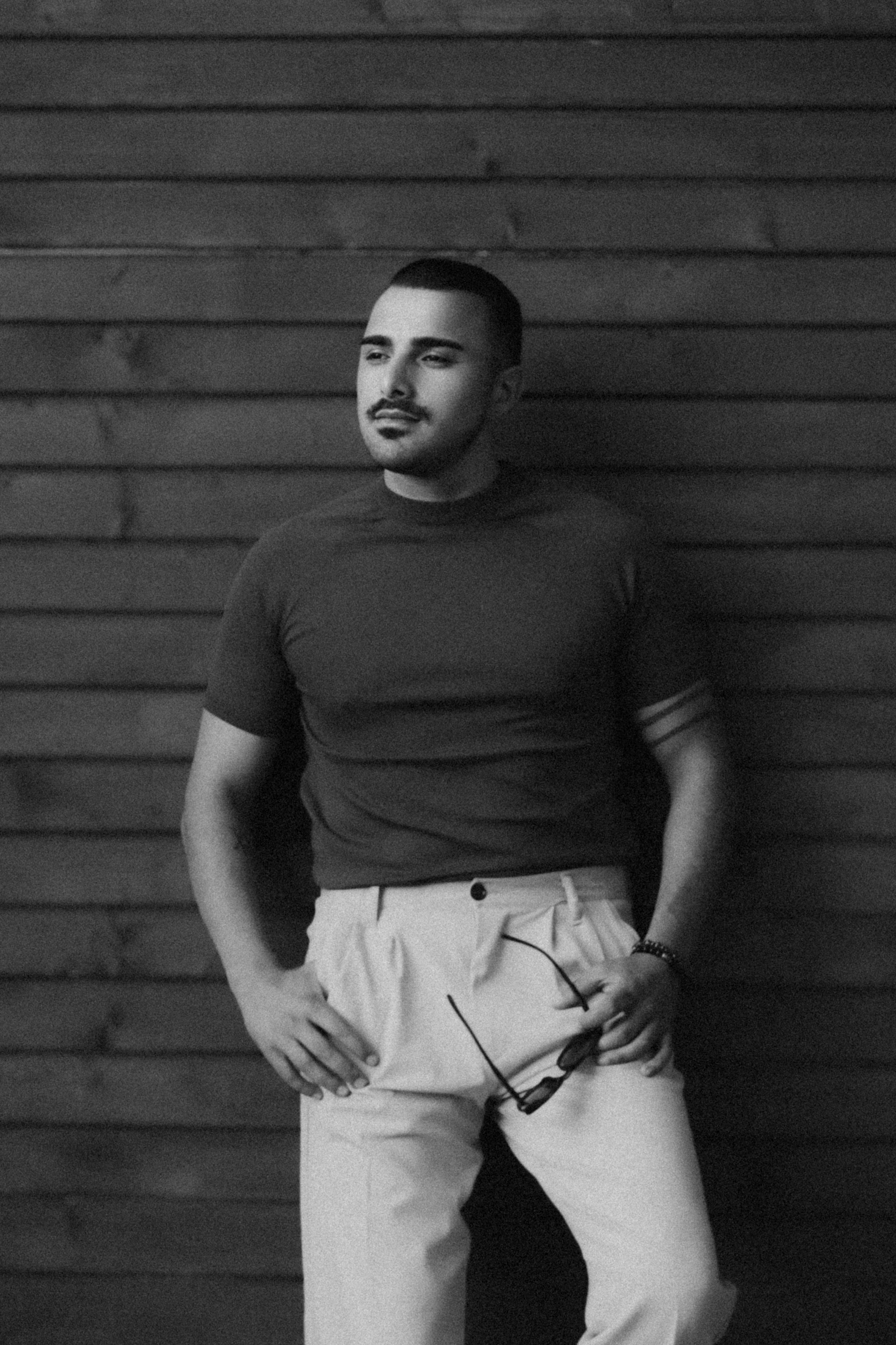Black and white photo of a stylish man posing with sunglasses and mustache.