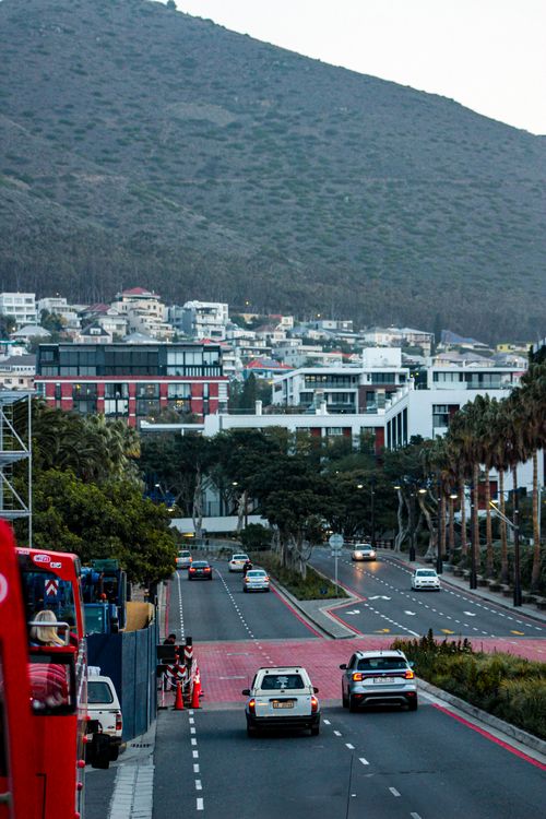 Free Scenic view of a city street with cars and modern buildings against a hillside, depicting urban life. Stock Photo