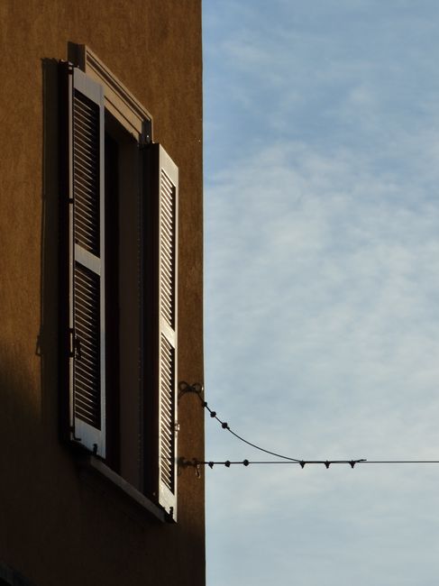 A window with open shutters in Milan, Lombardy against a clear sky.