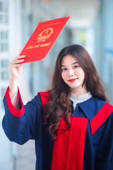 A young woman in a graduation gown holds a red diploma, celebrating her achievement.