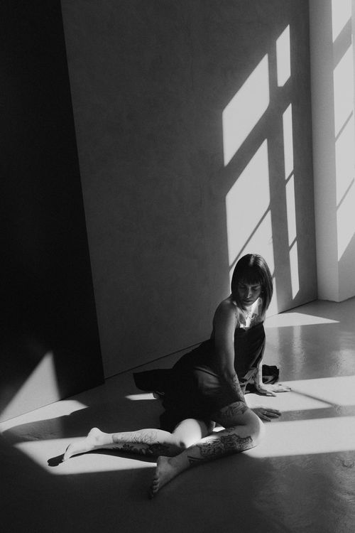 Free Black and white photo capturing a tattooed woman sitting in dramatic lighting indoors. Stock Photo