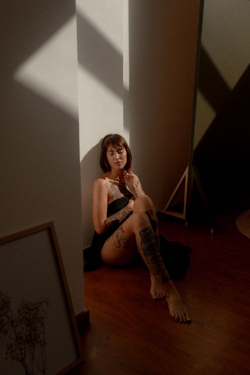 Free Artistic model sitting indoors with tattoos, captured in dramatic lighting. Stock Photo