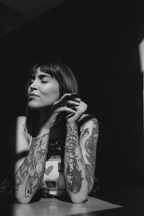 Free Black and white portrait of a tattooed woman with eyes closed and sunlit shadows. Stock Photo