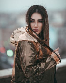 一位时尚女士身着透明雨衣，在户外摆出姿势，营造出现代艺术氛围