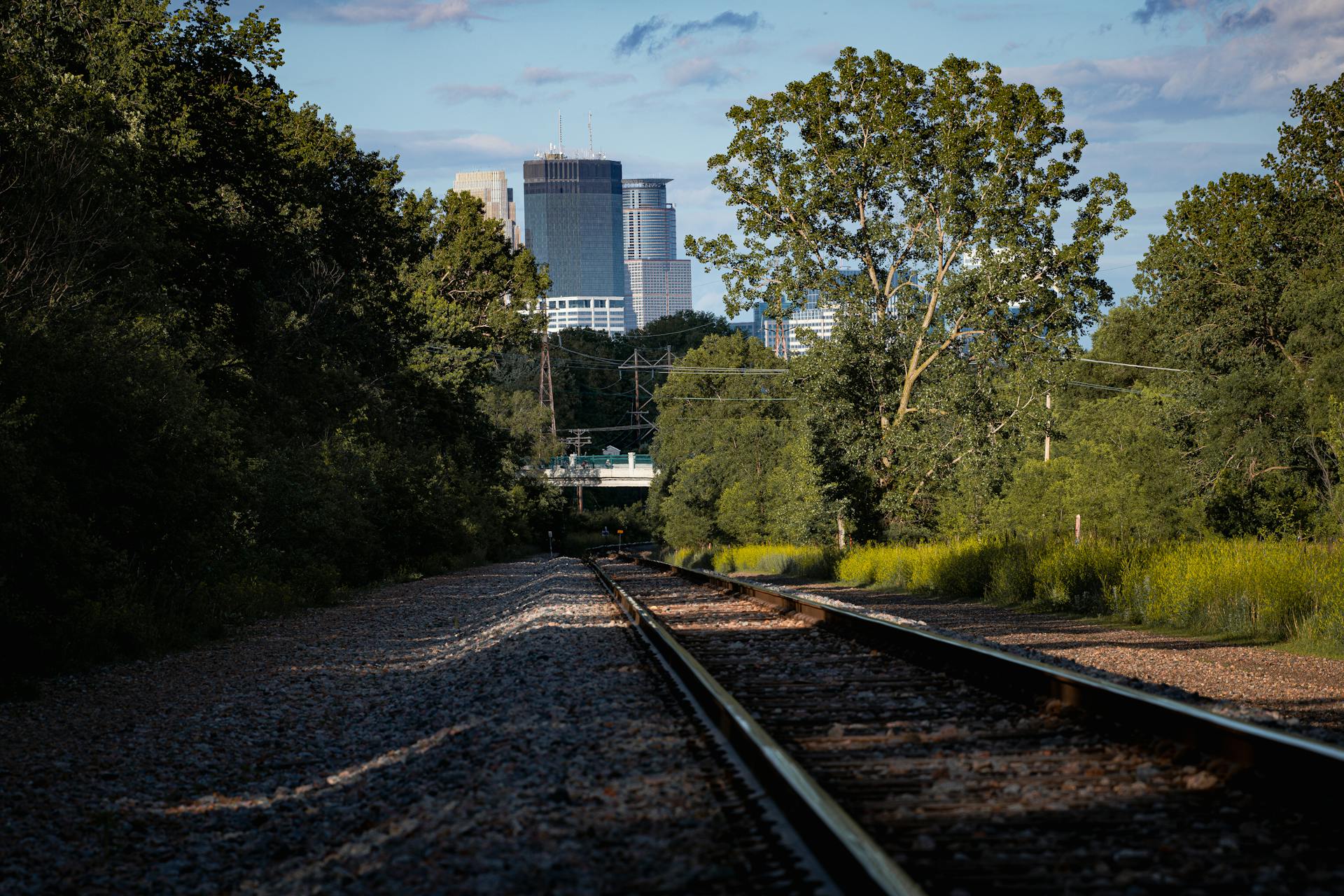 Railway tracks surrounded by greenery under a clear sky leading towards Minneapolis cityscape.
