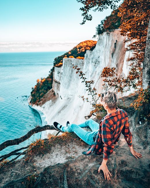 Person in plaid shirt enjoys a view from a clifftop overlooking a stunning coastline on a clear day.