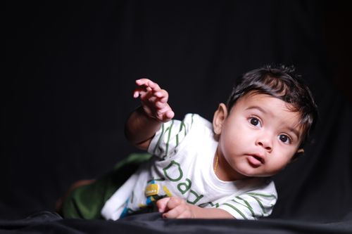 Free Cute baby boy crawling on a dark backdrop, capturing innocence and curiosity. Stock Photo