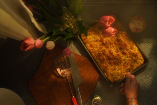 Top view of a tray of fresh focaccia bread with pink tulips and cutlery nearby.