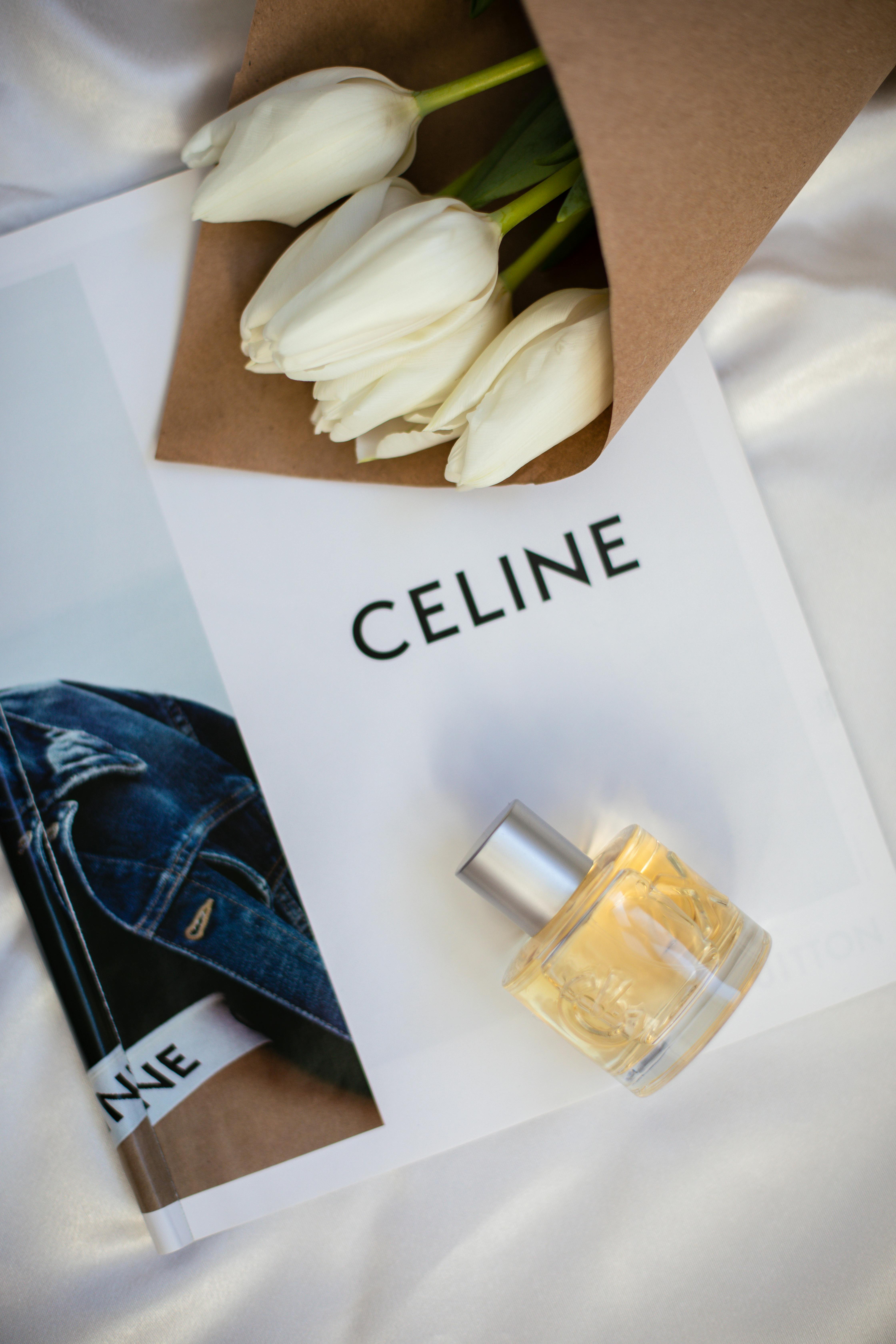 Stylish display of a perfume bottle, white tulips, and Celine book on silk fabric backdrop.