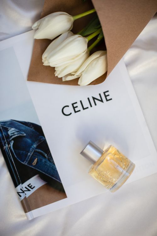 Free Stylish display of a perfume bottle, white tulips, and Celine book on silk fabric backdrop. Stock Photo