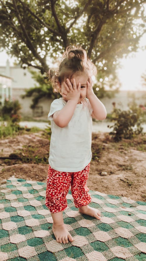 A little girl standing on a blanket with her hands covering her eyes