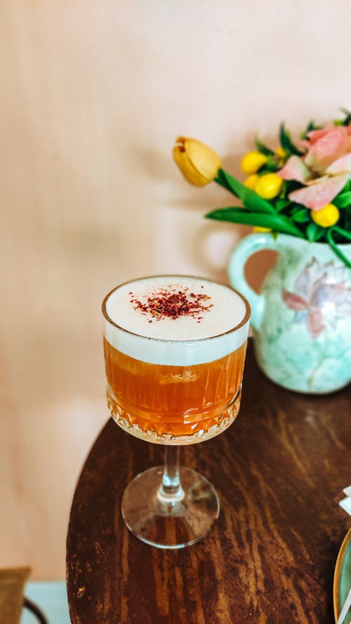 A glass of orange juice sitting on a table next to a vase of flowers