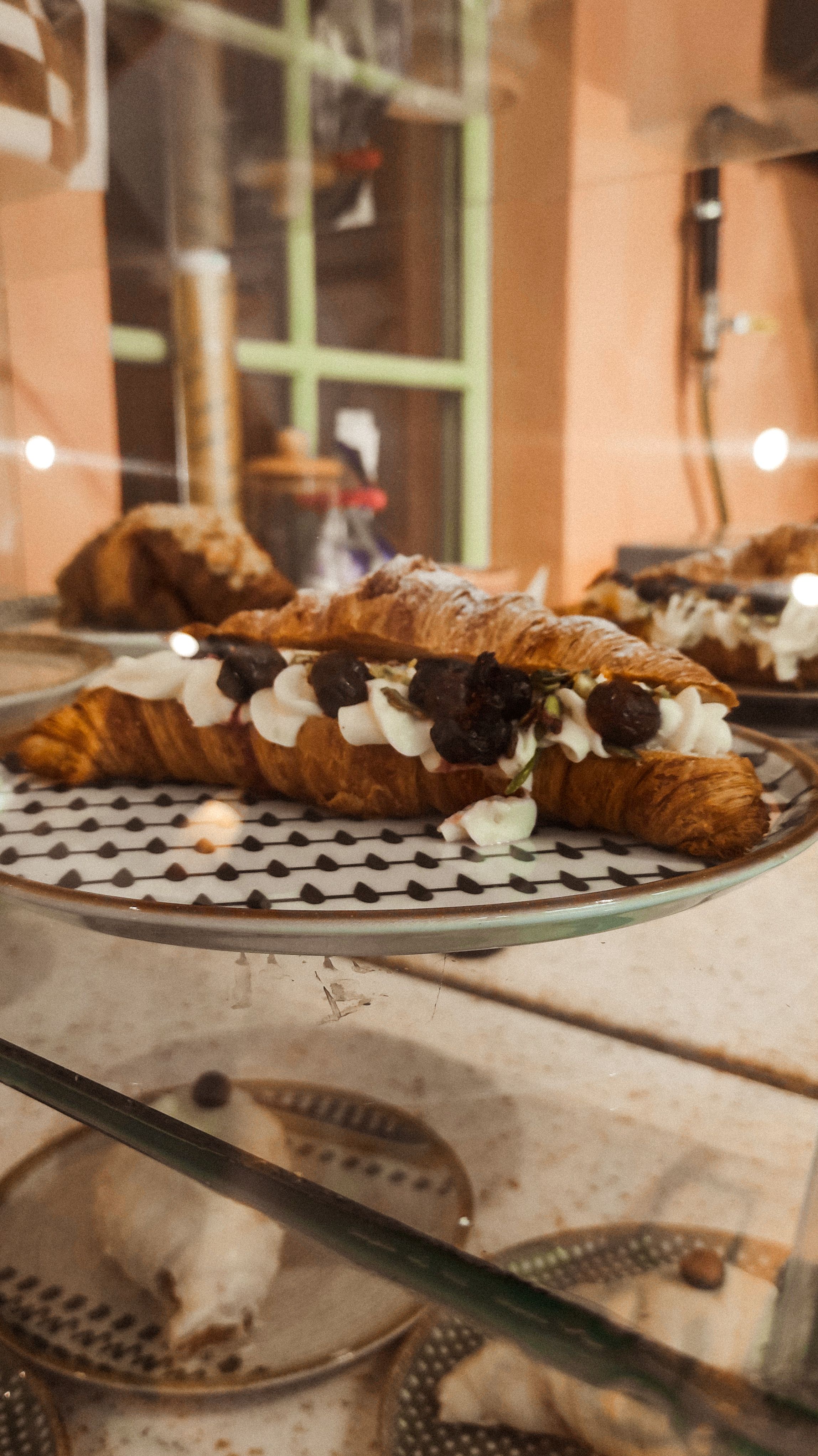 Close-up of a croissant topped with cream and chocolate on a patterned plate, elegant cafe setup.