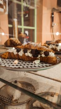 Close-up of a croissant topped with cream and chocolate on a patterned plate, elegant cafe setup.