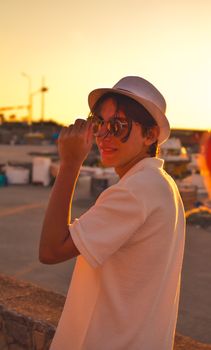 A fashionable woman in sunglasses and hat strolls along a scenic beach during sunset.