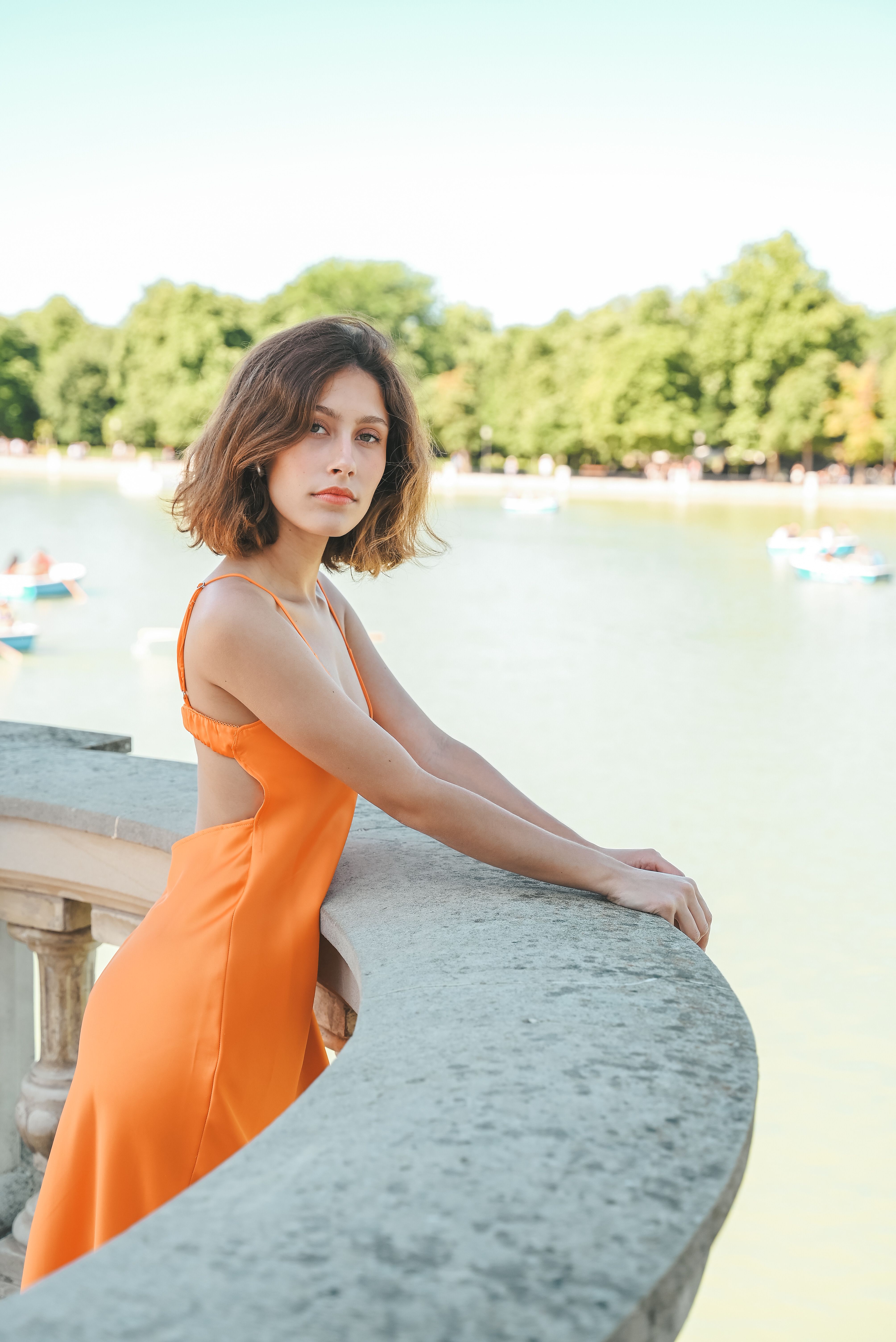 Woman in Orange Dress Leaning on Stone Railing by Lake · Free Stock Photo