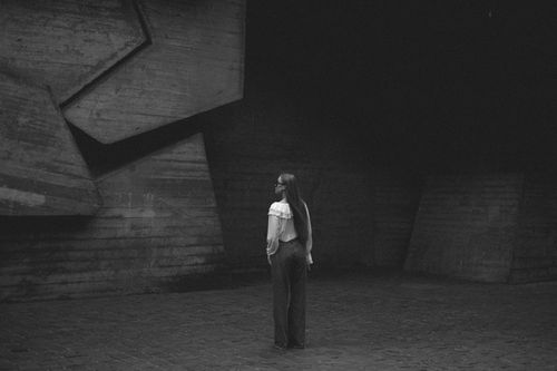 Free Woman with long hair in a stylish blouse stands against geometric concrete backdrop. Stock Photo