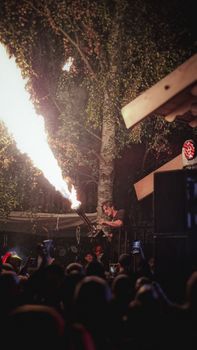 Dynamic scene of a performer wielding a fire cannon at a vibrant outdoor night event.