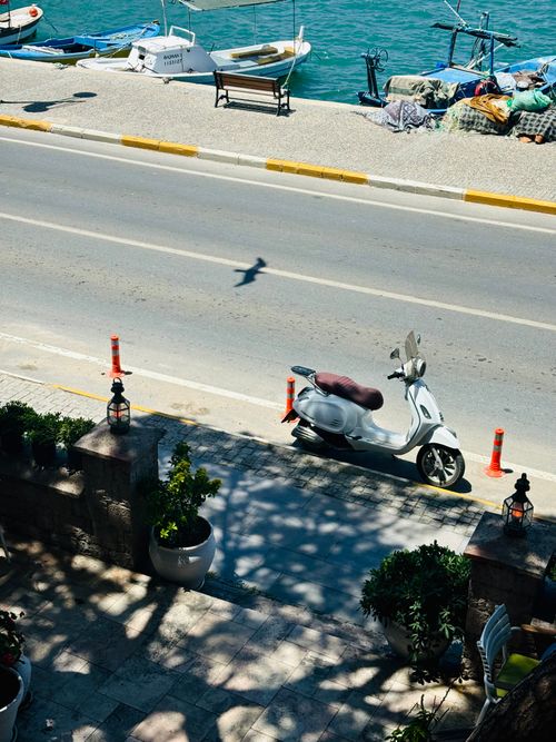 Free A city street with a parked scooter, overlooking a vibrant waterfront under clear skies. Stock Photo