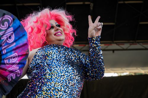 Free A glamorous drag queen with pink hair poses on stage holding a fan at a lively outdoor event. Stock Photo