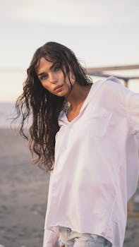A serene portrait of a woman in a white shirt posing on a sandy beach.