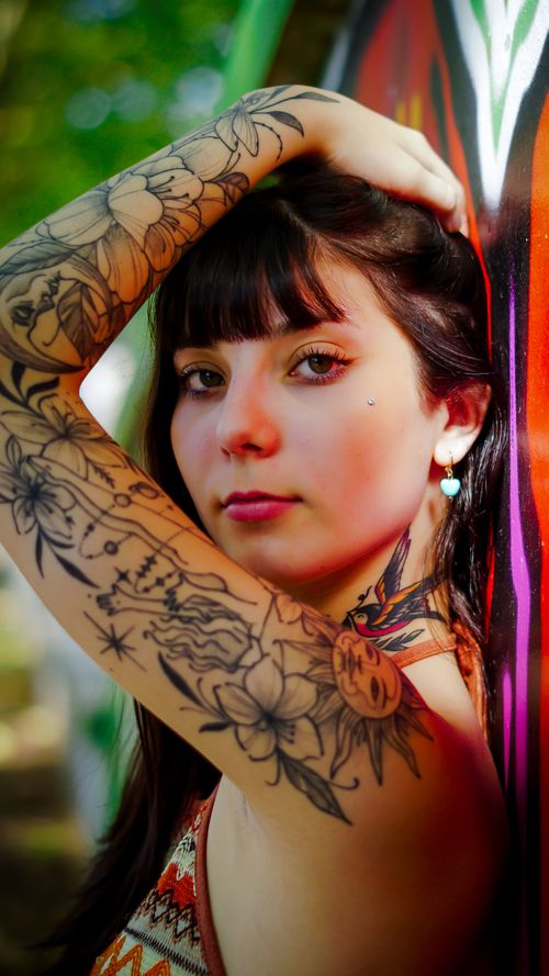 Free Close-up portrait of a tattooed woman with brunette hair leaning against a vibrant wall outdoors. Stock Photo