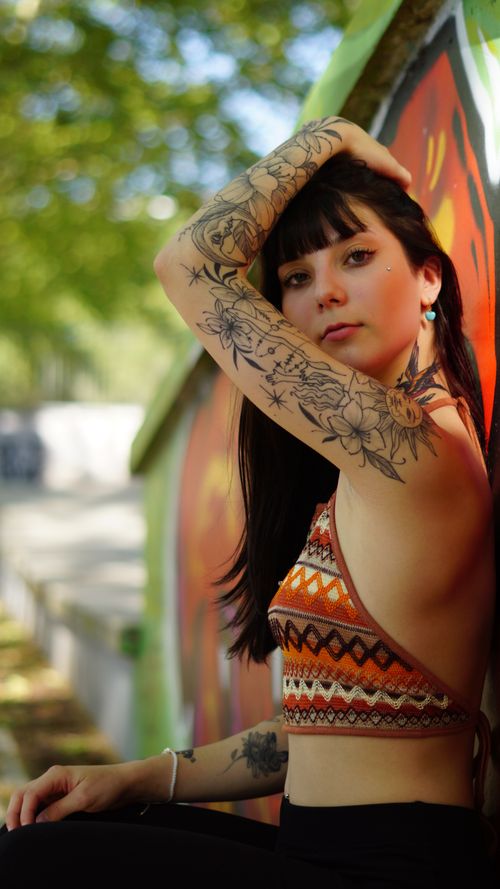Free Young tattooed woman in a crop top poses by a graffiti wall, highlighting artistic expression. Stock Photo