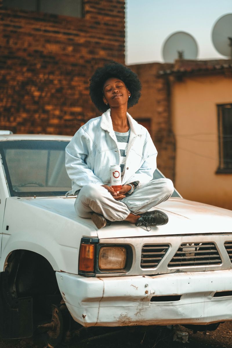 Woman sitting on the hood of a white pickup truck outside a brick building