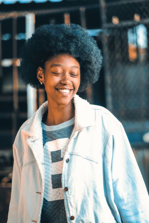 Free A young African American woman with afro smiling, eyes closed, wearing a denim jacket. Stock Photo