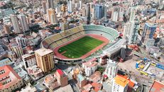 Aerial shot of a stadium in La Paz, Bolivia, surrounded by urban skyscrapers and cityscape.