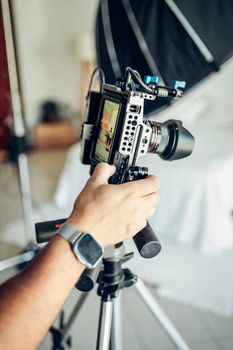 Close-up of a man's hand adjusting a digital camera mounted on a tripod in a photography studio environment.