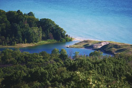 Free Explore a stunning aerial view of a forested lakeshore meeting clear blue waters, a perfect summer landscape. Stock Photo