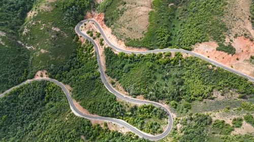 Free Aerial view of a winding road through lush hills and green vegetation in Utah's stunning landscape. Stock Photo