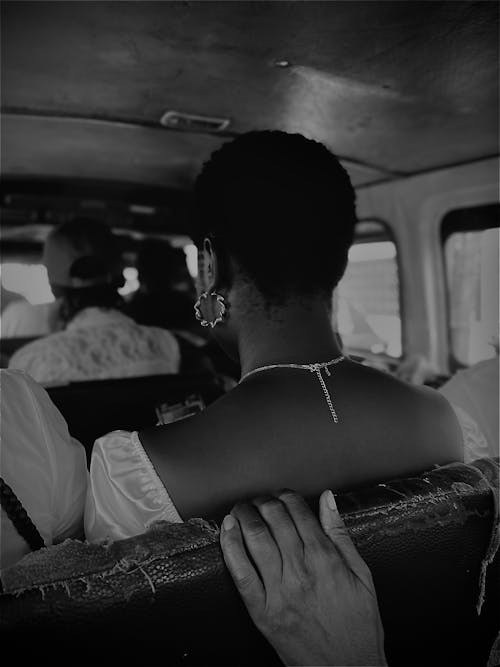 A black and white photo of a woman sitting in the back of a bus