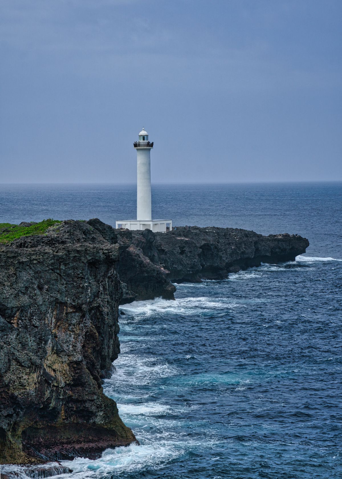 Cape Zanpa lighthouse towers over rocky coastline in southern Japan guiding ships through Pacific waters