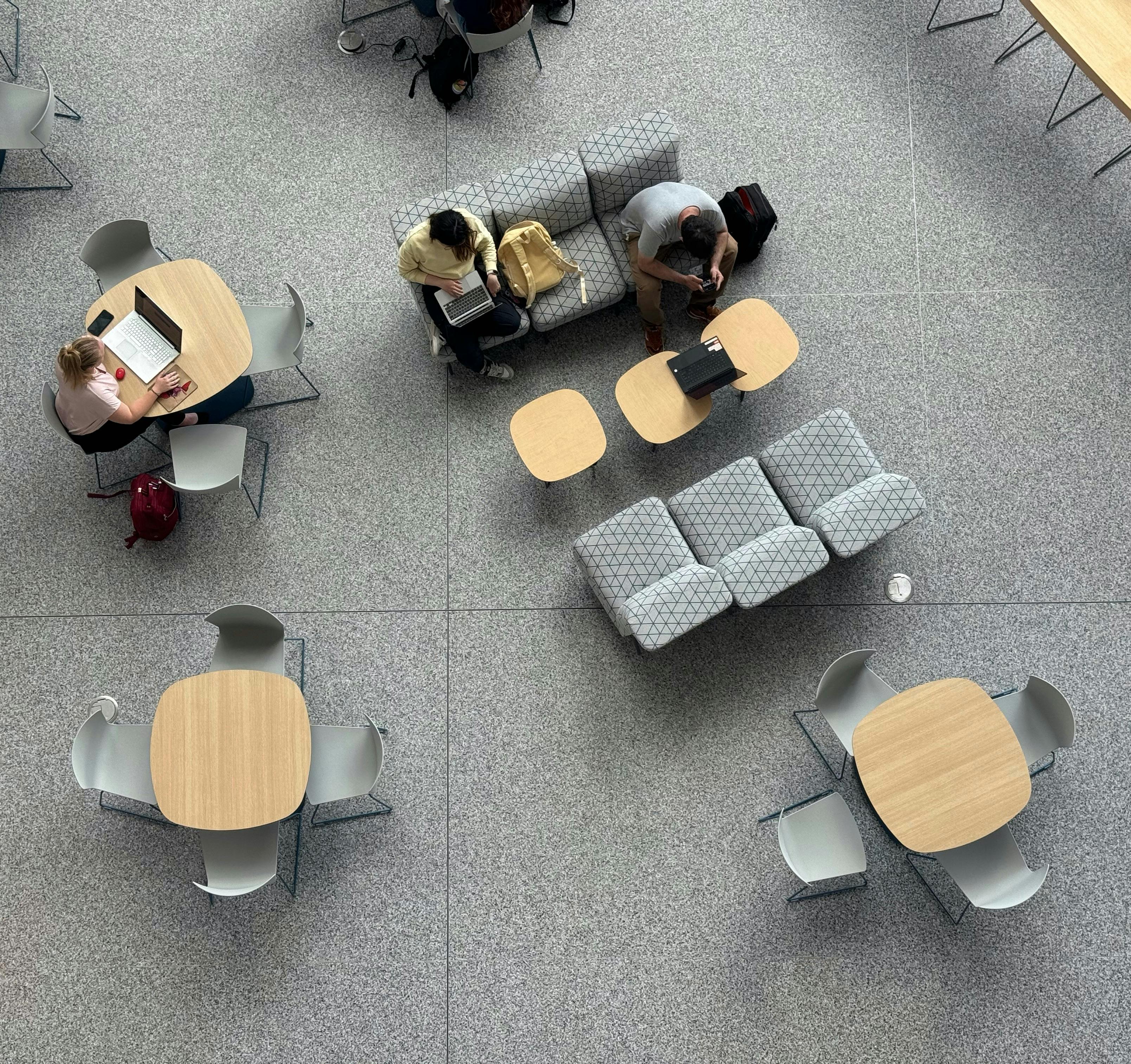 一张俯视图，展示人们在宽敞大厅的现代桌子上使用笔记本电脑工作。