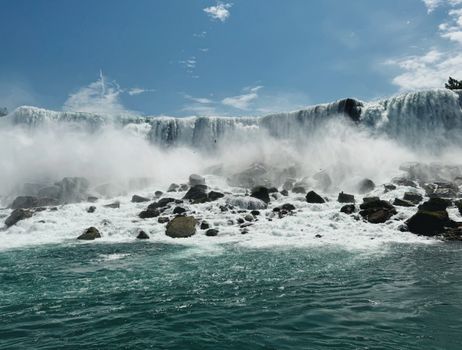 A breathtaking view of a powerful waterfall cascading over rocks under a clear blue sky.