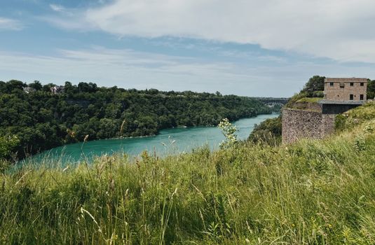 A serene landscape featuring a flowing river, lush greenery, and a historic fortress.